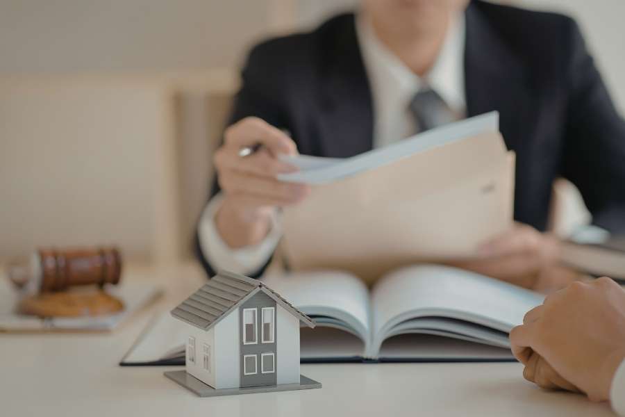 Conseiller en costume examinant des documents immobiliers avec une maquette de maison et un marteau de juge pour gérer sa fiscalité