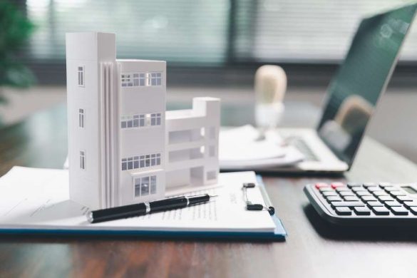 Maquette d'immeuble blanc posée sur des documents avec calculatrice et ordinateur pour gérer sa fiscalité immobilière