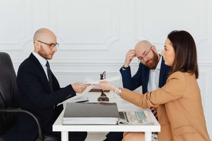 Une femme tend des documents à un conseiller lors d'un rendez-vous professionnel pour se faire indemniser.